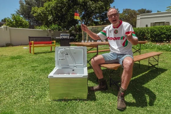 Jubelnde Person mit Deutschlandfahne und offener Kühlbox im Garten.